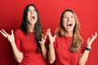 © Krakenimages.com - Hispanic family of mother and daughter wearing casual clothes over red background crazy and mad shouting and yelling with aggressive expression and arms raised. frustration concept.