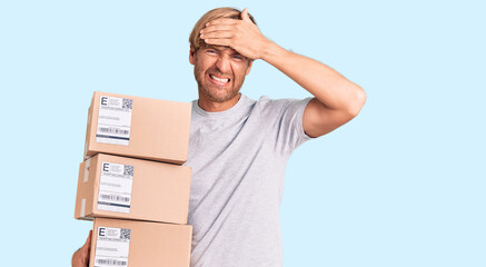 Poster - Handsome caucasian man with beard holding delivery packages stressed and frustrated with hand on head, surprised and angry face