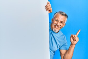 Sticker - Middle age grey-haired man holding blank empty banner smiling happy pointing with hand and finger to the side