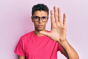 Wall Mural - Young handsome african american man wearing glasses over pink background doing stop sing with palm of the hand. warning expression with negative and serious gesture on the face.