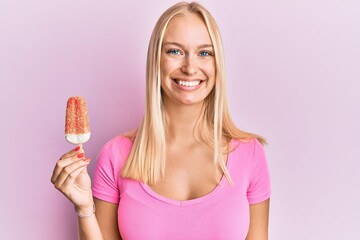 Sticker - Young blonde girl holding ice cream looking positive and happy standing and smiling with a confident smile showing teeth