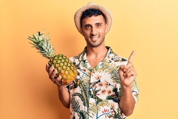 Poster - Young hispanic man wearing summer hat holding pineapple smiling happy pointing with hand and finger to the side