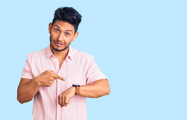 Handsome latin american young man wearing casual summer shirt in hurry pointing to watch time, impatience, upset and angry for deadline delay