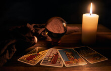 Concept Of Fortune-telling Wooden Table And White Candle With A Crystal Ball And Tarot Cards On Dark Background    
