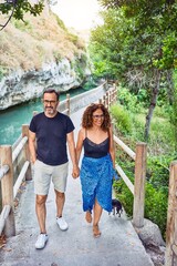 Wall Mural - Middle age couple smiling happy walking with chihuahua dog around beautiful landscape at the park