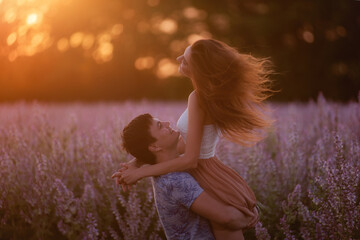 Young man took beautiful woman in his arms, whirls her around blooming purple sage field in the rays of the sunset. The girl's hair is flying in different directions. An offer of marriage. Copy space