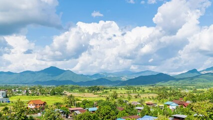 Wall Mural - Beautiful rice paddy farming filed and village town at Pua district during harvest season with Doi Phu Kha mountain in background, Nan province, Thailand - time lapse