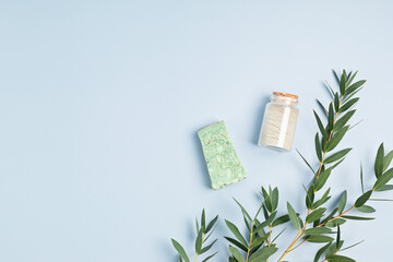 Wall Mural - Cosmetics branding mockup. Bottles of essential oil, sea salt, soap bar, fresh eucalyptus branches on blue background. Natual organic ingredients for skin care, body treatment, beauty product concept