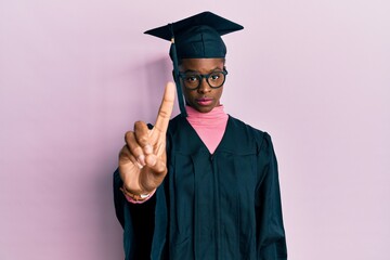 Canvas Print - Young african american girl wearing graduation cap and ceremony robe pointing with finger up and angry expression, showing no gesture