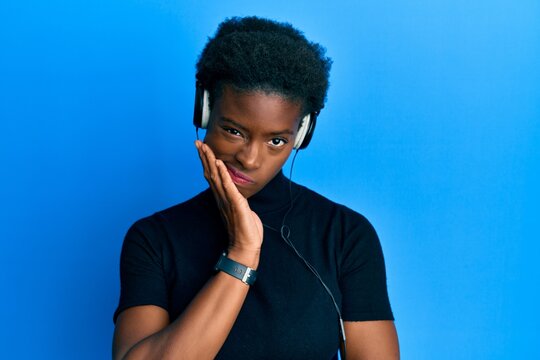 Young african american girl listening to music using headphones thinking looking tired and bored with depression problems with crossed arms.