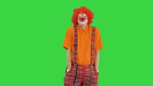 Clown Wearing A Red Nose Holding His Hands In Pockets While Looking Into The Camera On A Green Screen, Chroma Key.