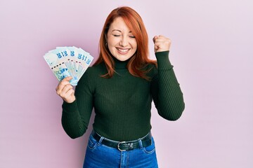 Poster - Beautiful redhead woman holding 20 hong kong dollars banknotes screaming proud, celebrating victory and success very excited with raised arm