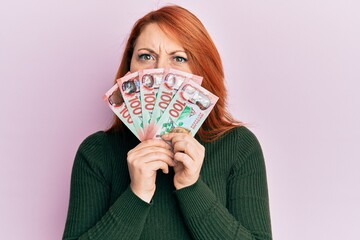 Sticker - Beautiful redhead woman holding 100 new zealand dollars banknote skeptic and nervous, frowning upset because of problem. negative person.