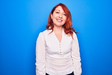 Poster - Young beautiful redhead businesswoman wearing elegant shirt standing over blue background with a happy and cool smile on face. Lucky person.