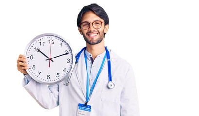 Poster - Handsome hispanic man wearing doctor uniform holding clock looking positive and happy standing and smiling with a confident smile showing teeth