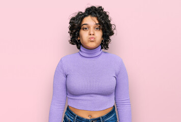 Young hispanic woman with curly hair wearing casual clothes puffing cheeks with funny face. mouth inflated with air, crazy expression.