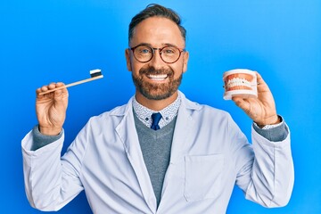 Sticker - Handsome middle age dentist man holding denture and toothbrush smiling with a happy and cool smile on face. showing teeth.