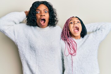 Poster - Beautiful african american mother and daughter wearing casual winter sweater crazy and scared with hands on head, afraid and surprised of shock with open mouth