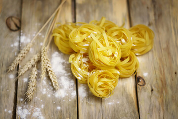 Selective focus. Fettuccine pasta on a wooden surface. Flour and ears of wheat. The concept of making pasta from durum wheat.