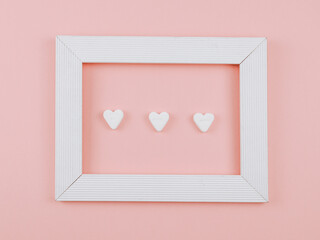 Wall Mural - frame with heart.
Three hearts in a white frame on a pink background, close-up top view.