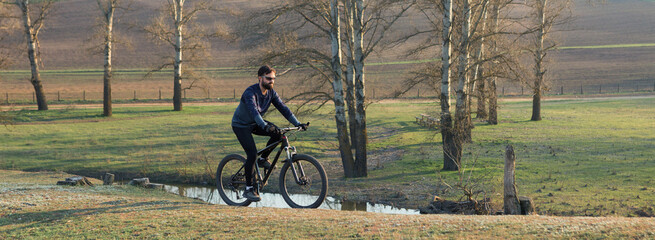 Cyclist in shorts and jersey on a modern carbon hardtail bike with an air suspension fork standing on a cliff against the background of fresh green spring forest