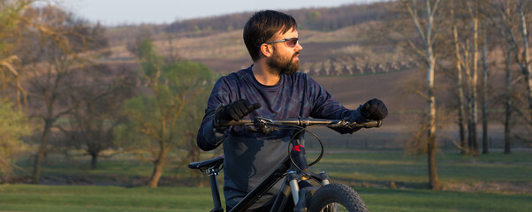 Cyclist in shorts and jersey on a modern carbon hardtail bike with an air suspension fork standing on a cliff against the background of fresh green spring forest