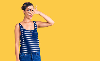 Sticker - Young beautiful woman wearing casual clothes and glasses peeking in shock covering face and eyes with hand, looking through fingers with embarrassed expression.