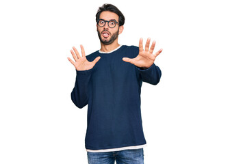 Sticker - Young hispanic man wearing casual clothes and glasses afraid and terrified with fear expression stop gesture with hands, shouting in shock. panic concept.