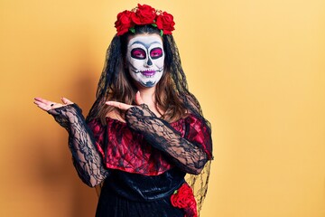 Sticker - Young woman wearing day of the dead costume over yellow amazed and smiling to the camera while presenting with hand and pointing with finger.