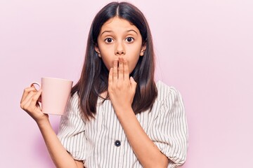 Poster - Beautiful child girl holding coffee covering mouth with hand, shocked and afraid for mistake. surprised expression