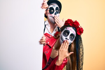 Sticker - Couple wearing day of the dead costume holding blank empty banner covering mouth with hand, shocked and afraid for mistake. surprised expression