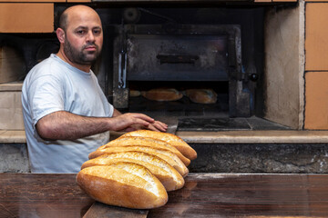 Baker. A young handsome bakery worker on the background of bread, takes bread from a stove with a wooden shovel. Industrial production of bakery products. a man in the baker's special clothing. Bakery