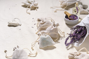 Hand made lavender sachets in small bags and cotton hearts on textile tablecloth. Dry lavender flowers in tracing paper and jar. Glass bottle with lavender oil. Natural homemade gifts.