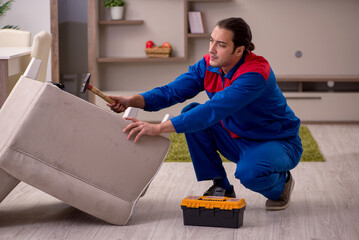 Young male contractor repairing arm-chair indoors