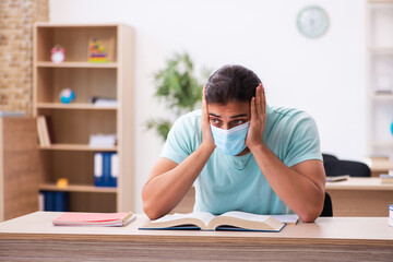 Young male student sitting in the classroom wearing mask