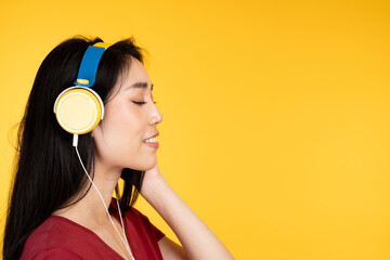 Portrait of beautiful Asian Woman joyful listening to music on yellow headphone. Woman with happy smile listening popular song via headphones. Teenage girl wearing red t-shirt, listening to music.