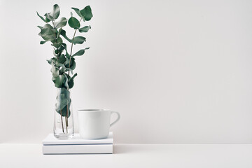 Wall Mural - A mug on a stack of books and a transparent vase with eucalyptus branches. Eco-friendly materials in interior decor, minimalism. Copy space, mock up