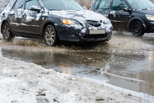 The Splashes Water From Under The Wheels Of A Vehicle Moving Through Spring Dirty Puddles From Melted Snow. Flood Waters.