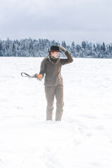 Wall Mural - A young beautiful hunter woman on the watching wild animals in the snowy landscape . There's a lot of snow all around and strong winds. In the background are trees.