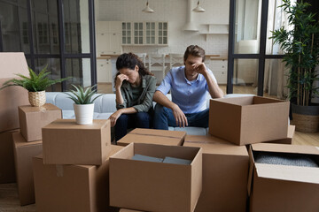 Fototapete - Tired unhappy young Caucasian couple sit on sofa in new living room feel unmotivated unpacking. Upset stressed millennial man and woman have fight quarrel unboxing packages relocating moving.
