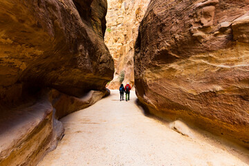 Wall Mural - (Selective focus) Stunning view of a couple in the distance walking on the path leading to Al Khazneh (The Treasury). Petra is a historical and archaeological city in southern Jordan.