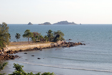 A jetty with tropical palm trees jutting out from the beach into the ocean with islands visable on the horizon 