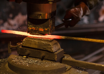 Close up blacksmith forging a red-hot iron billet on an automatic wall. Handicraft concept