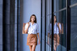 © visoot - Happy woman holding shopping bag walking and using a smart phone in the street in a sunny summer day
