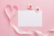 White blank sheet of paper and pink ribbon in the shape of a heart on a pink background. Valentine's day concept.