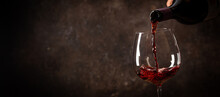 Pouring Red Wine Into The Glass Against Rustic Dark Wooden Background