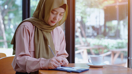 Young beautiful Asian Muslim women enjoying a relaxing moment working and playing with mobile phone in the coffee shop on a bright sunny day