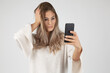 © MrsLePew - studios shot Beautiful young blond woman in casual outfit taking selfie mit mobile phone and hand in hair