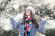 Portrait shot of attractive young woman wearing hat and winter coat while standing outside and enjoy falling snow. Happy woman standing outdoor and raising her hands while snowing heavily 
