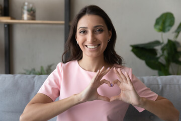 Close up portrait of smiling young indian Arabic woman show heart love hand gesture support sick. Happy millennial middle eastern female feel supportive, show empathy and care. Volunteer concept.